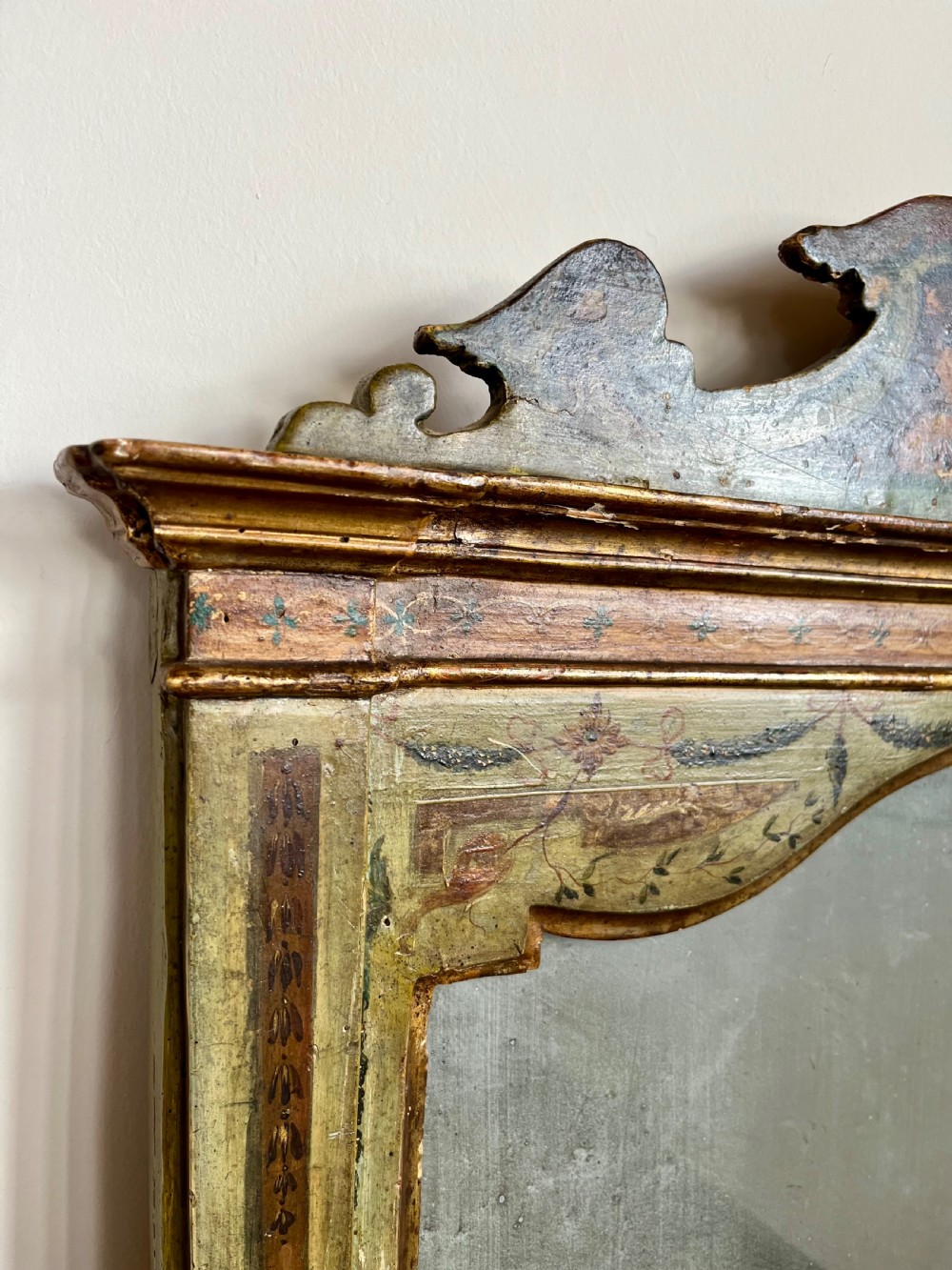 A rectangular painted wooden wall mirror featuring a carved scrolled pediment, an arched inner frame, and painted foliage motifs on a green background. View II