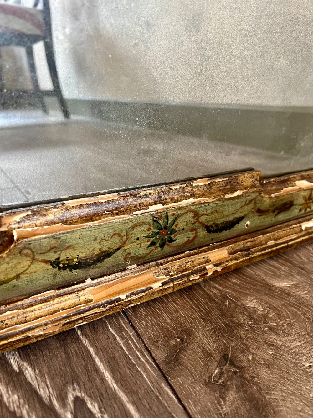 A rectangular painted wooden wall mirror featuring a carved scrolled pediment, an arched inner frame, and painted foliage motifs on a green background. View V