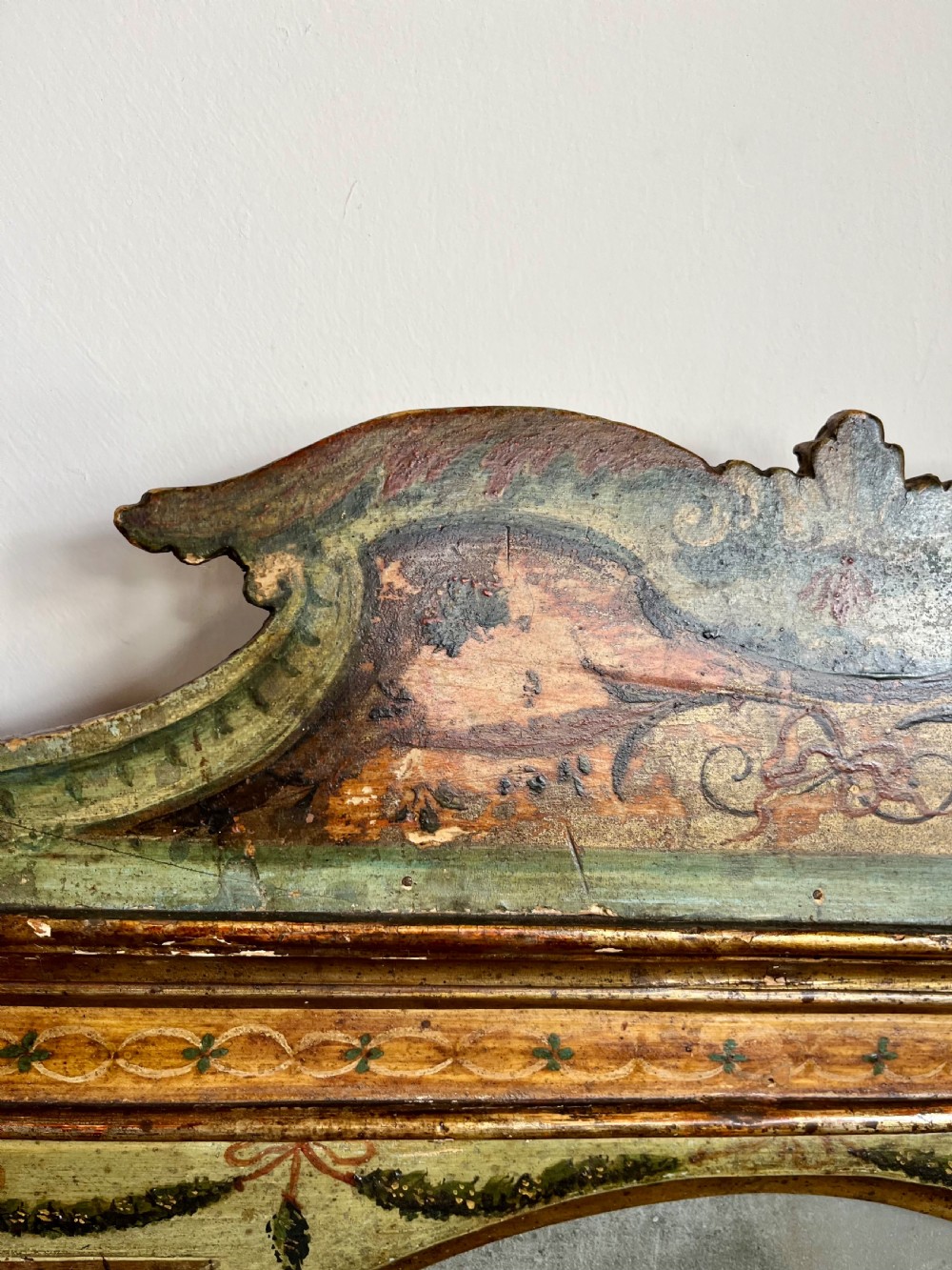 A rectangular painted wooden wall mirror featuring a carved scrolled pediment, an arched inner frame, and painted foliage motifs on a green background. View VI