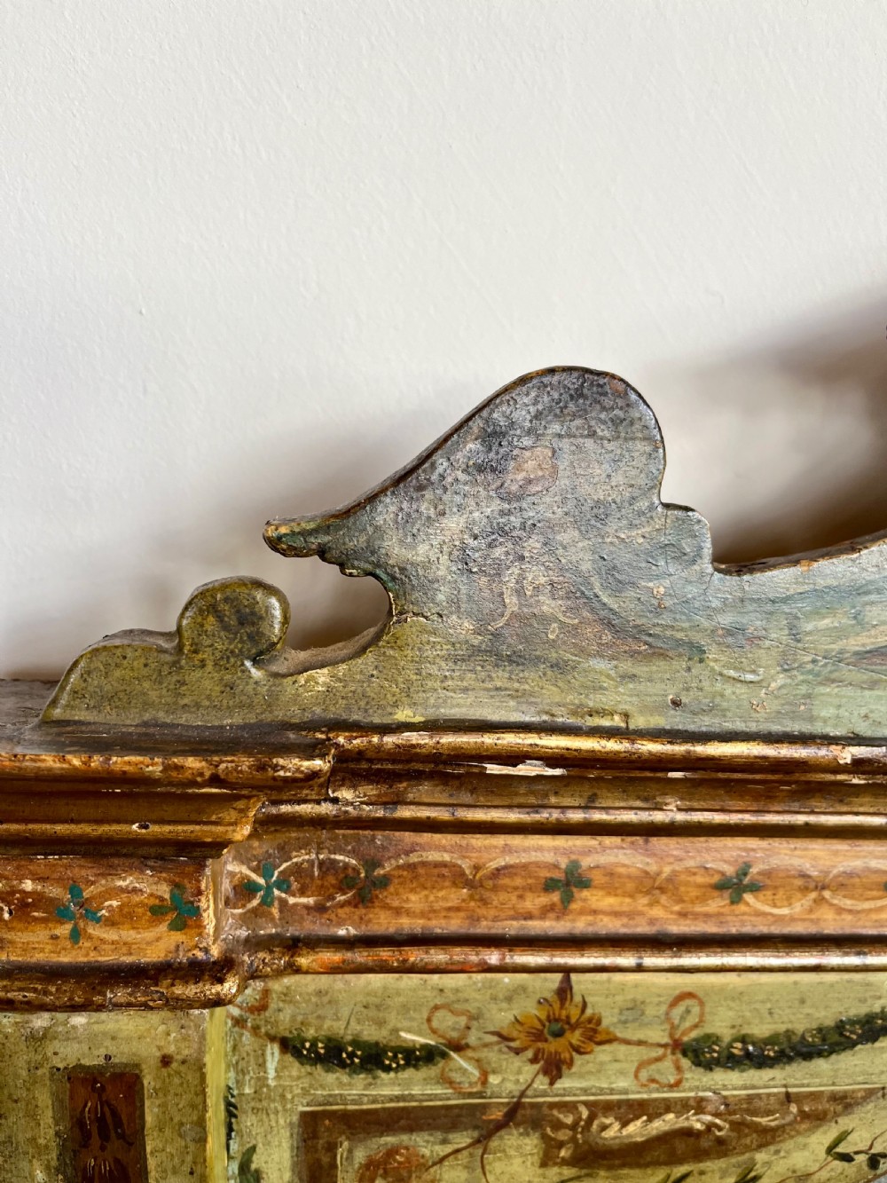 A rectangular painted wooden wall mirror featuring a carved scrolled pediment, an arched inner frame, and painted foliage motifs on a green background. View VII