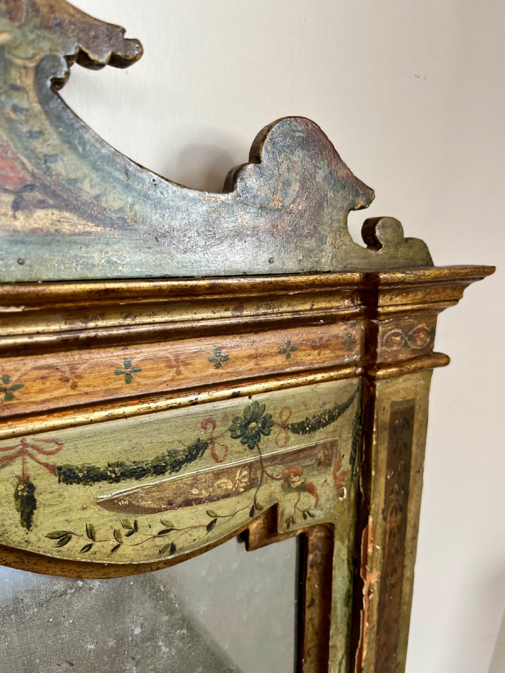 A rectangular painted wooden wall mirror featuring a carved scrolled pediment, an arched inner frame, and painted foliage motifs on a green background. View VIII