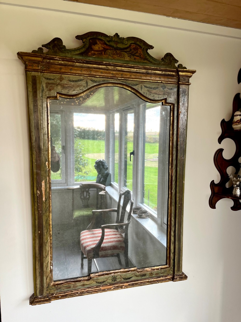 A rectangular painted wooden wall mirror featuring a carved scrolled pediment, an arched inner frame, and painted foliage motifs on a green background. View XIII
