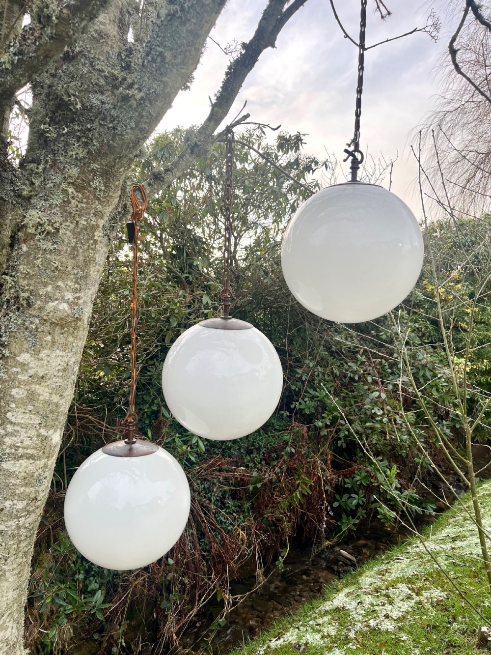 A set of three large white spherical opaline glass globe pendant lights suspended from dark metal chains.