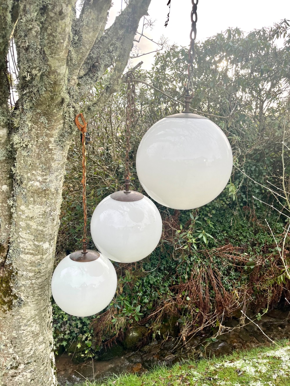 A set of three large white spherical opaline glass globe pendant lights suspended from dark metal chains. View V