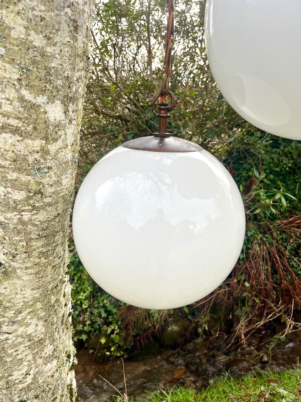 A set of three large white spherical opaline glass globe pendant lights suspended from dark metal chains. View VI
