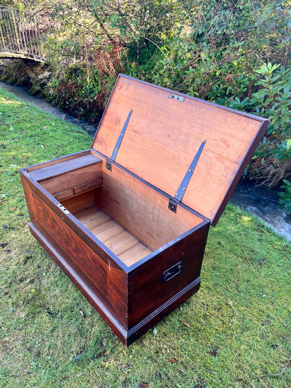 A rectangular dark reddish-brown pine storage chest with a hinged lid, painted panel border detail, and iron side handles. View VII