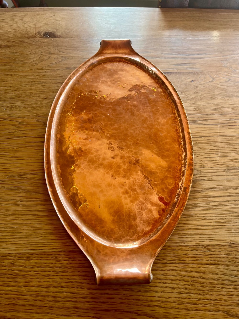 A large oval hand-hammered copper serving tray featuring integrated raised handles at both ends.