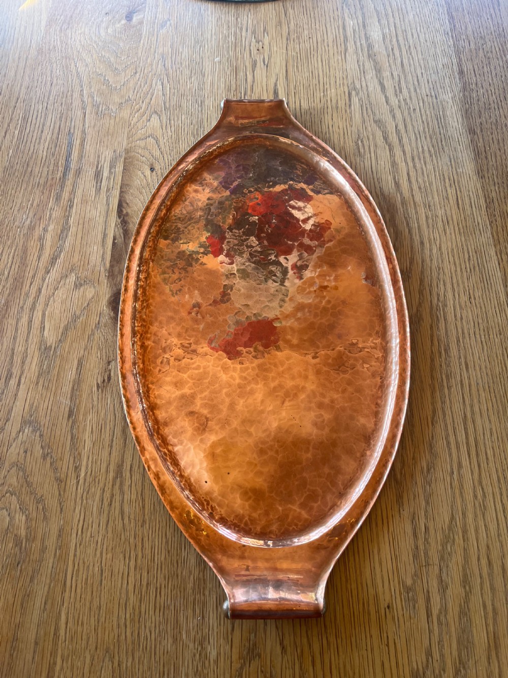 A large oval hand-hammered copper serving tray featuring integrated raised handles at both ends. View III