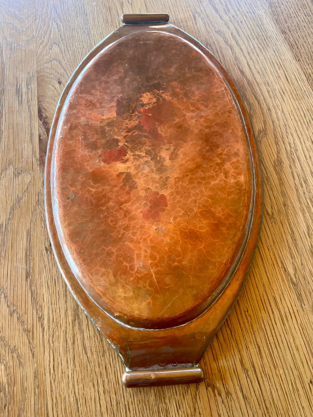 A large oval hand-hammered copper serving tray featuring integrated raised handles at both ends. View VII