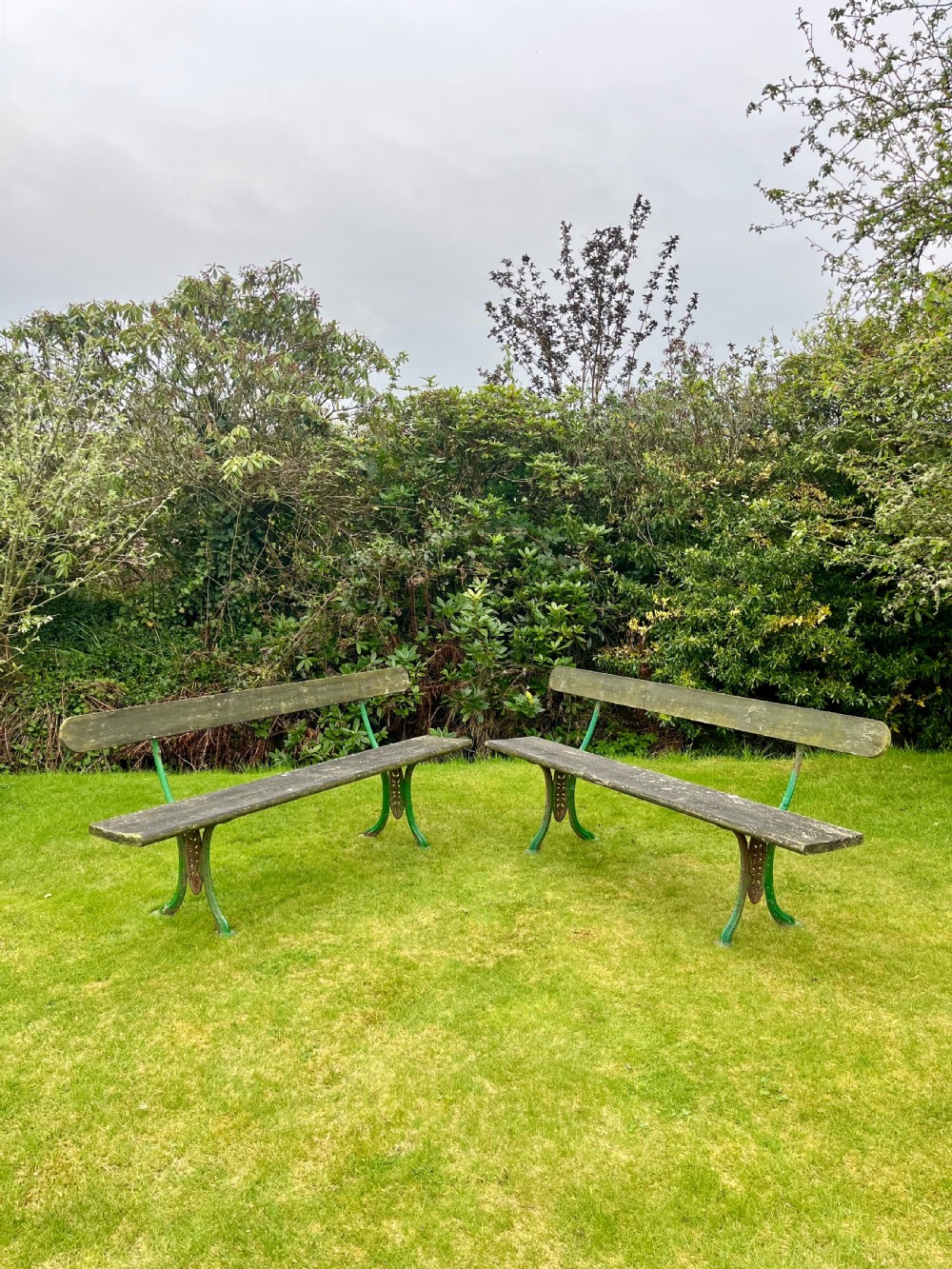 A pair of outdoor garden benches featuring green painted cast iron legs supporting weathered wooden plank seats and backrests.