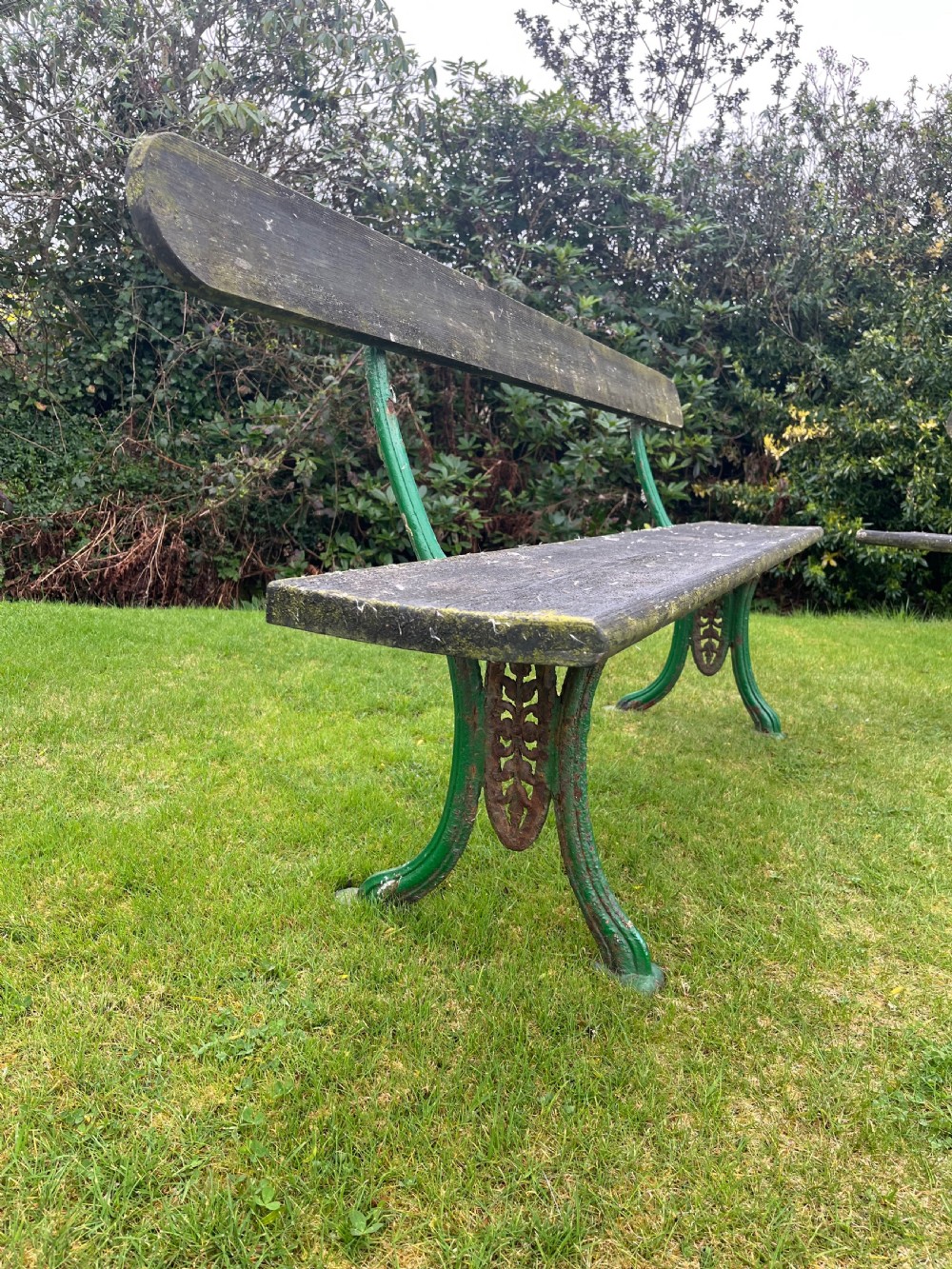 A pair of outdoor garden benches featuring green painted cast iron legs supporting weathered wooden plank seats and backrests. View II