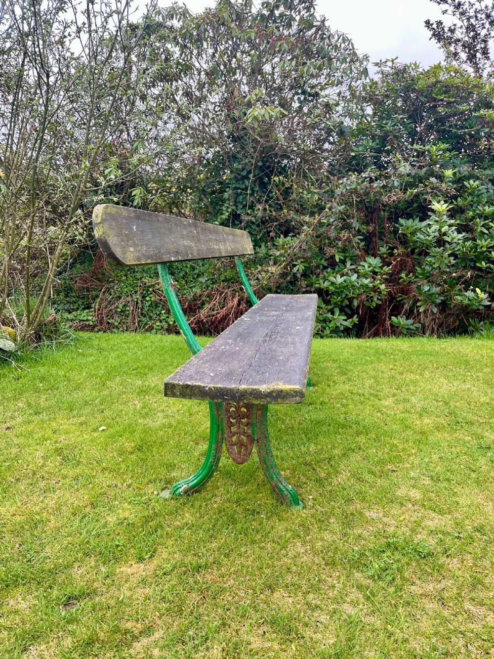 A pair of outdoor garden benches featuring green painted cast iron legs supporting weathered wooden plank seats and backrests. View III
