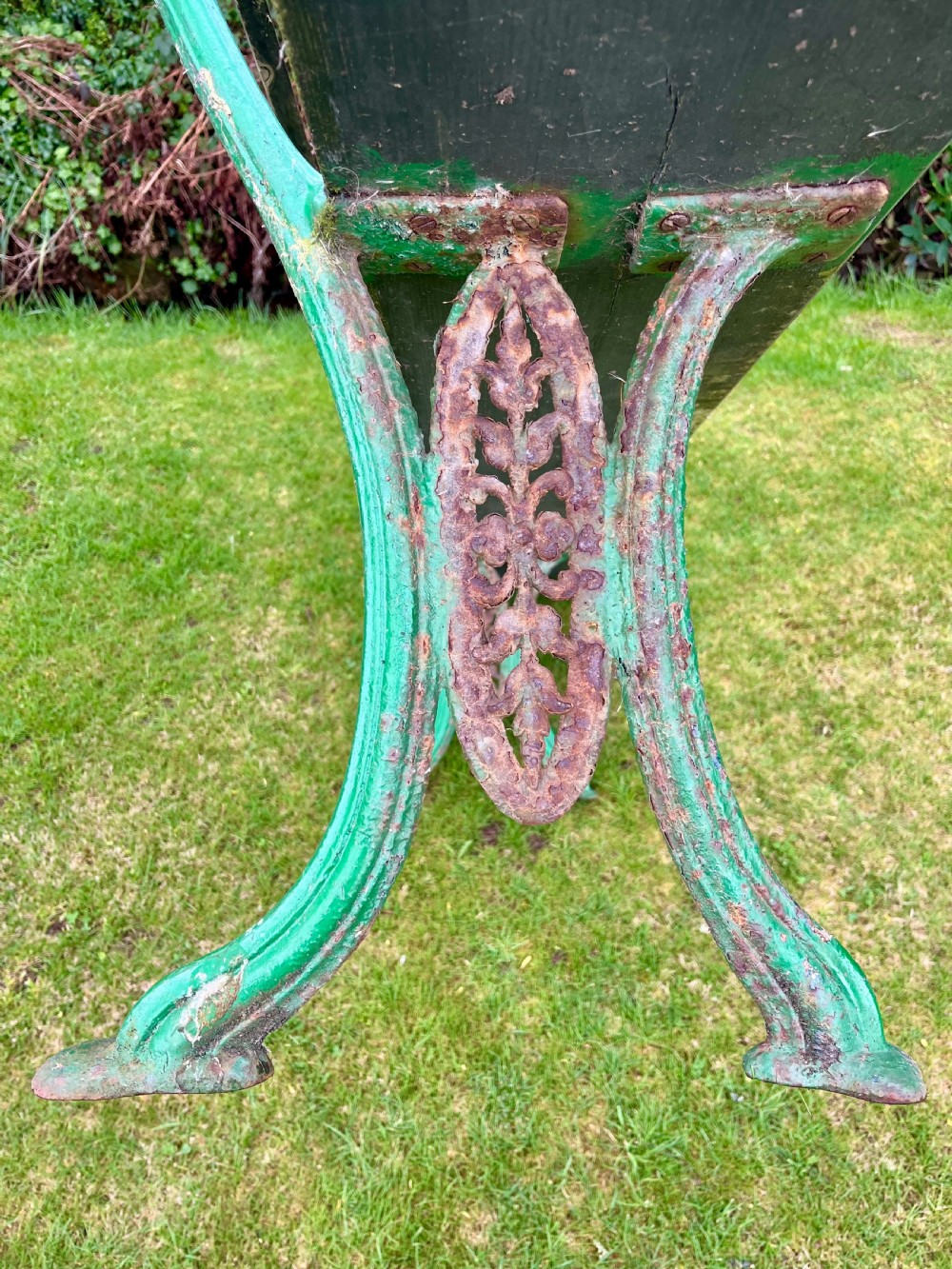 A pair of outdoor garden benches featuring green painted cast iron legs supporting weathered wooden plank seats and backrests. View IV