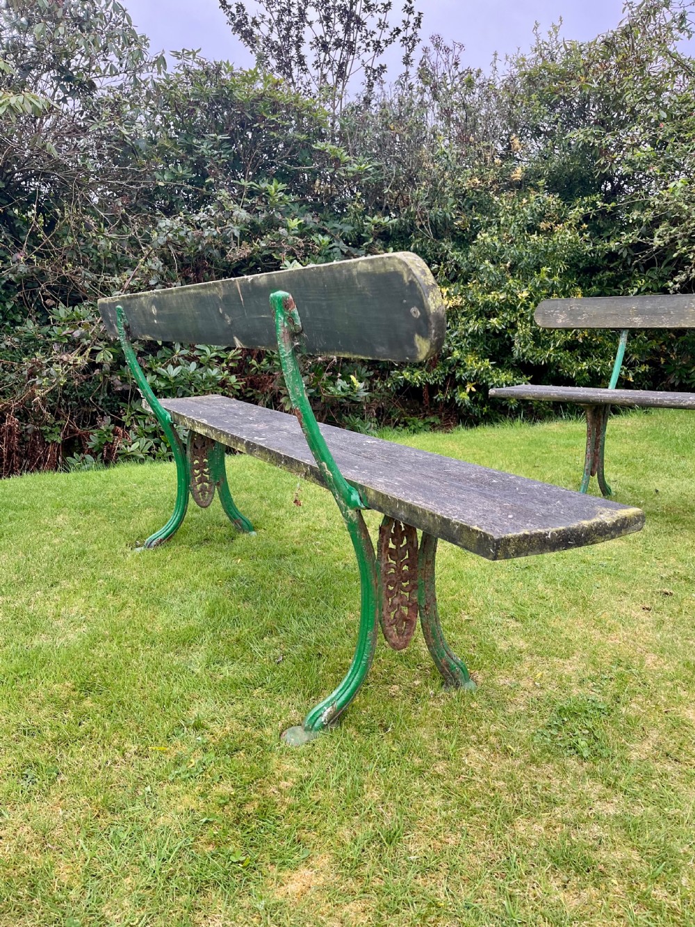 A pair of outdoor garden benches featuring green painted cast iron legs supporting weathered wooden plank seats and backrests. View V