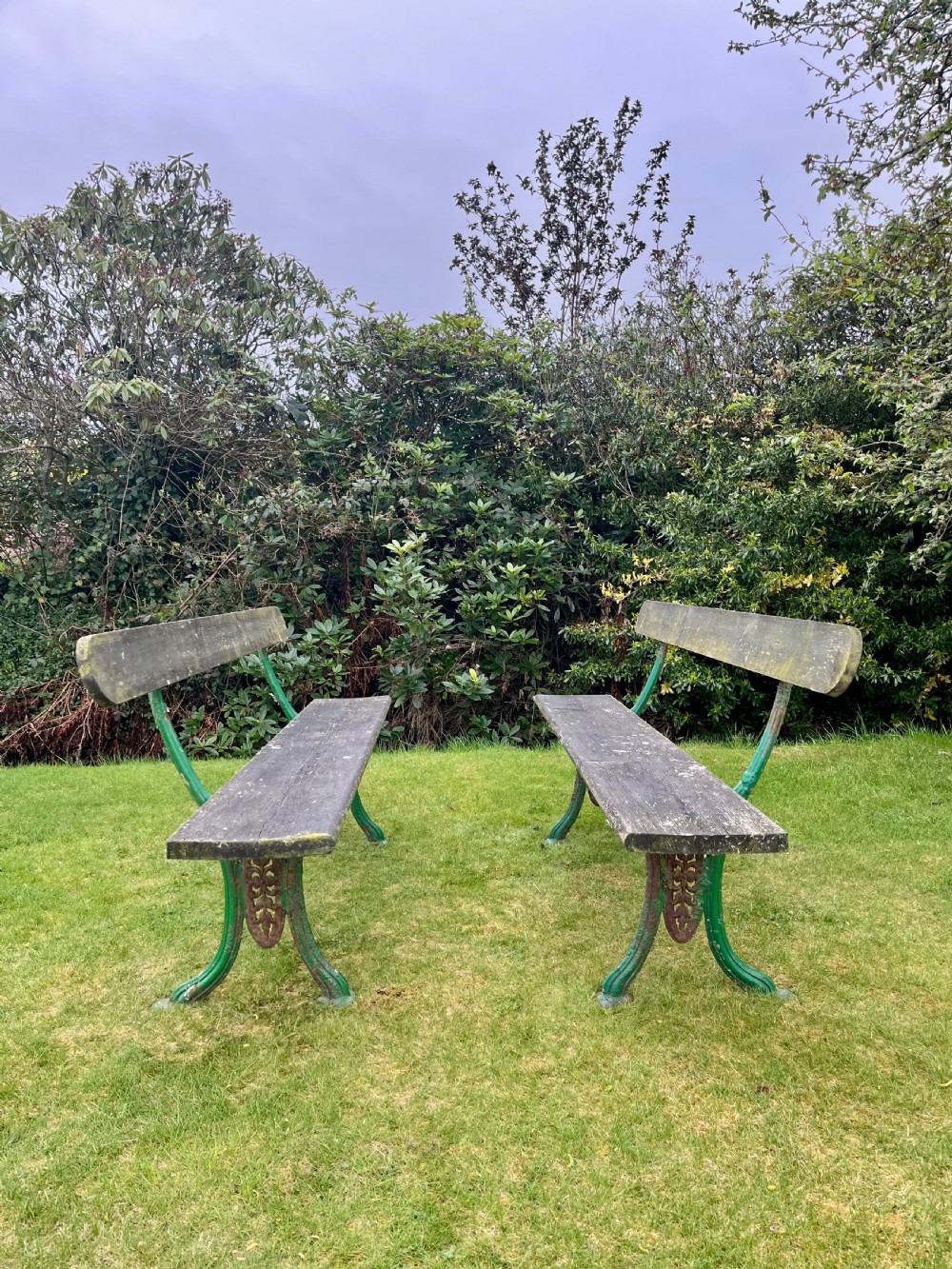 A pair of outdoor garden benches featuring green painted cast iron legs supporting weathered wooden plank seats and backrests. View VI