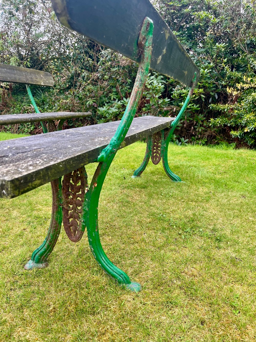 A pair of outdoor garden benches featuring green painted cast iron legs supporting weathered wooden plank seats and backrests. View VII