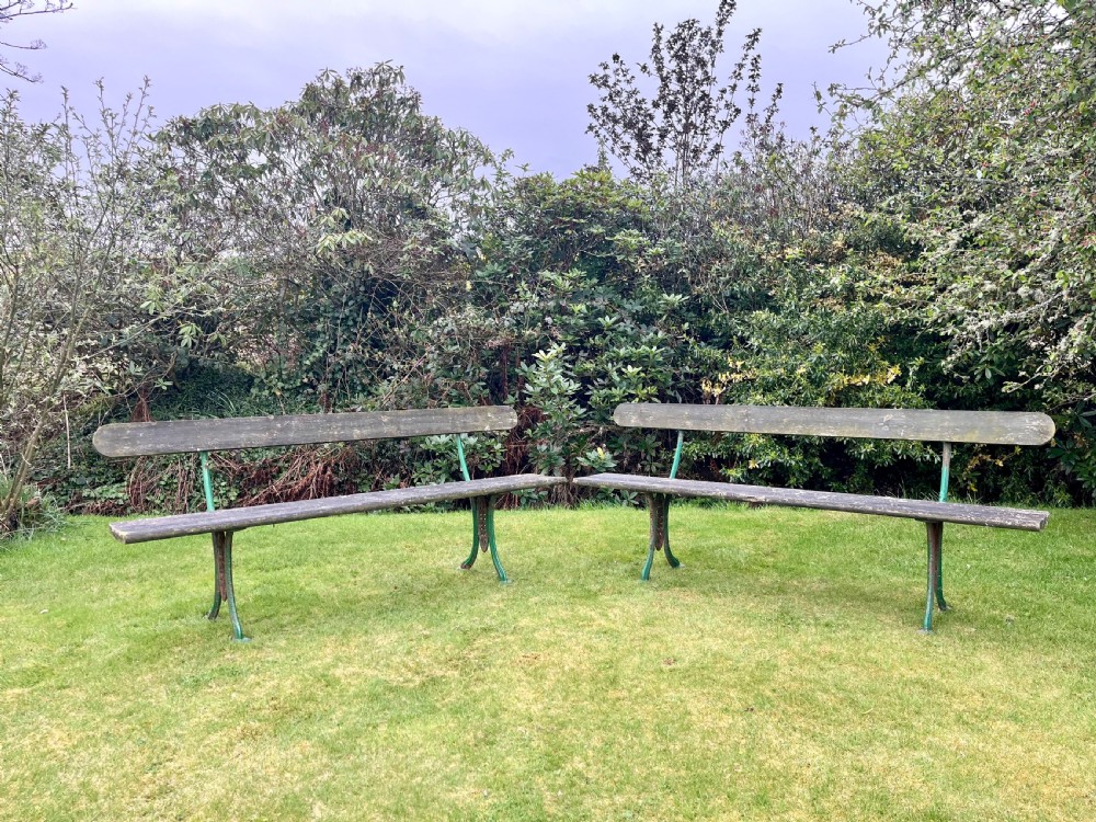 A pair of outdoor garden benches featuring green painted cast iron legs supporting weathered wooden plank seats and backrests. View IX
