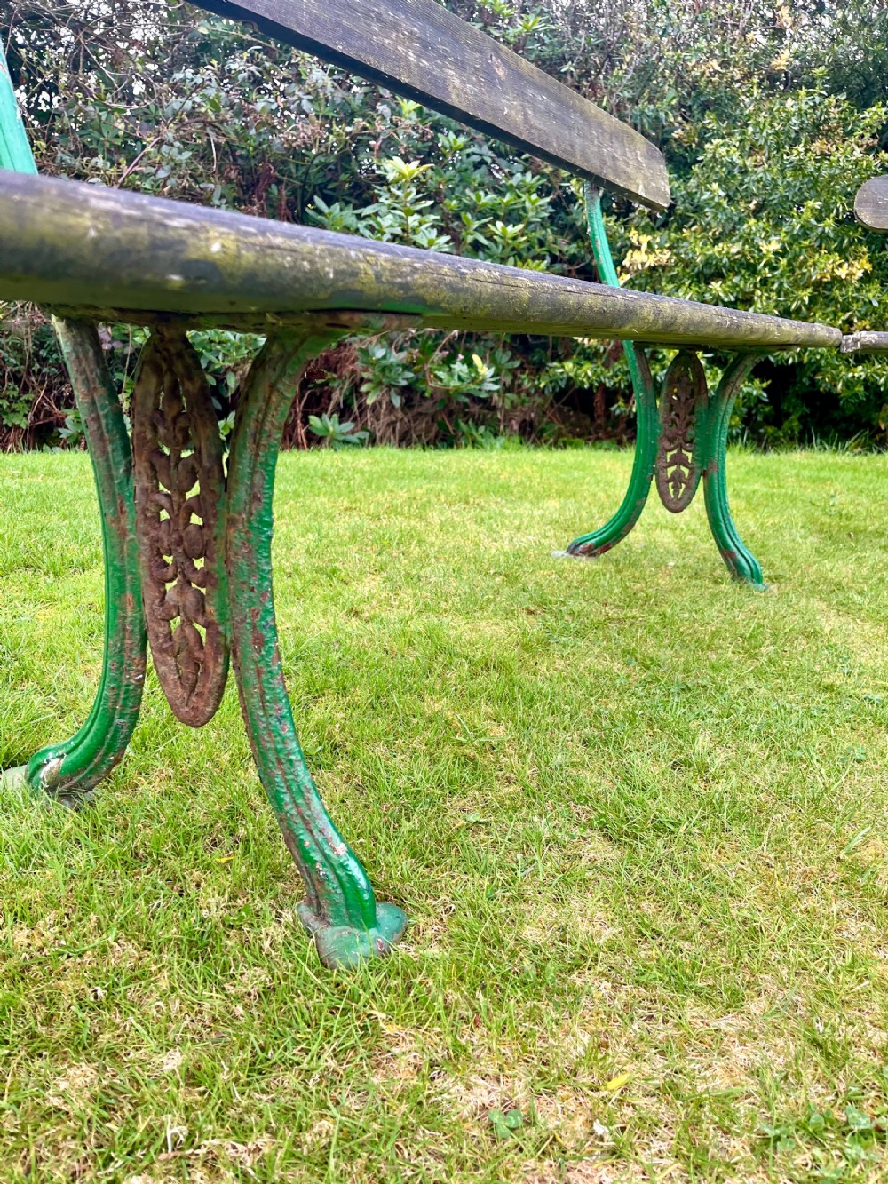 A pair of outdoor garden benches featuring green painted cast iron legs supporting weathered wooden plank seats and backrests. View X