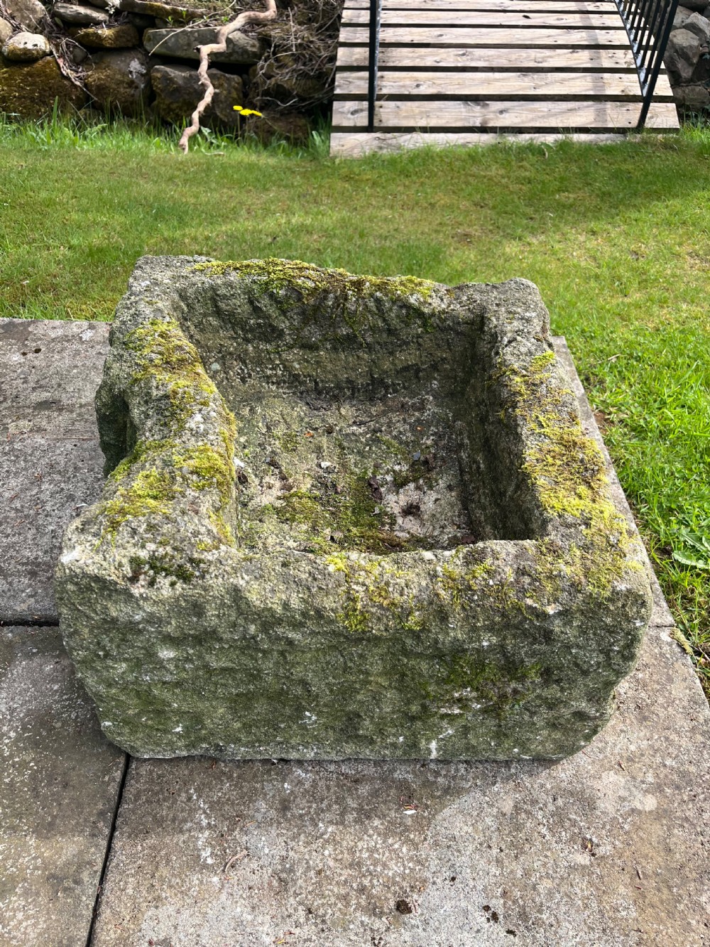 A rectangular hand-carved grey stone garden trough with a moss-covered weathered surface and a hollowed-out central basin. View II