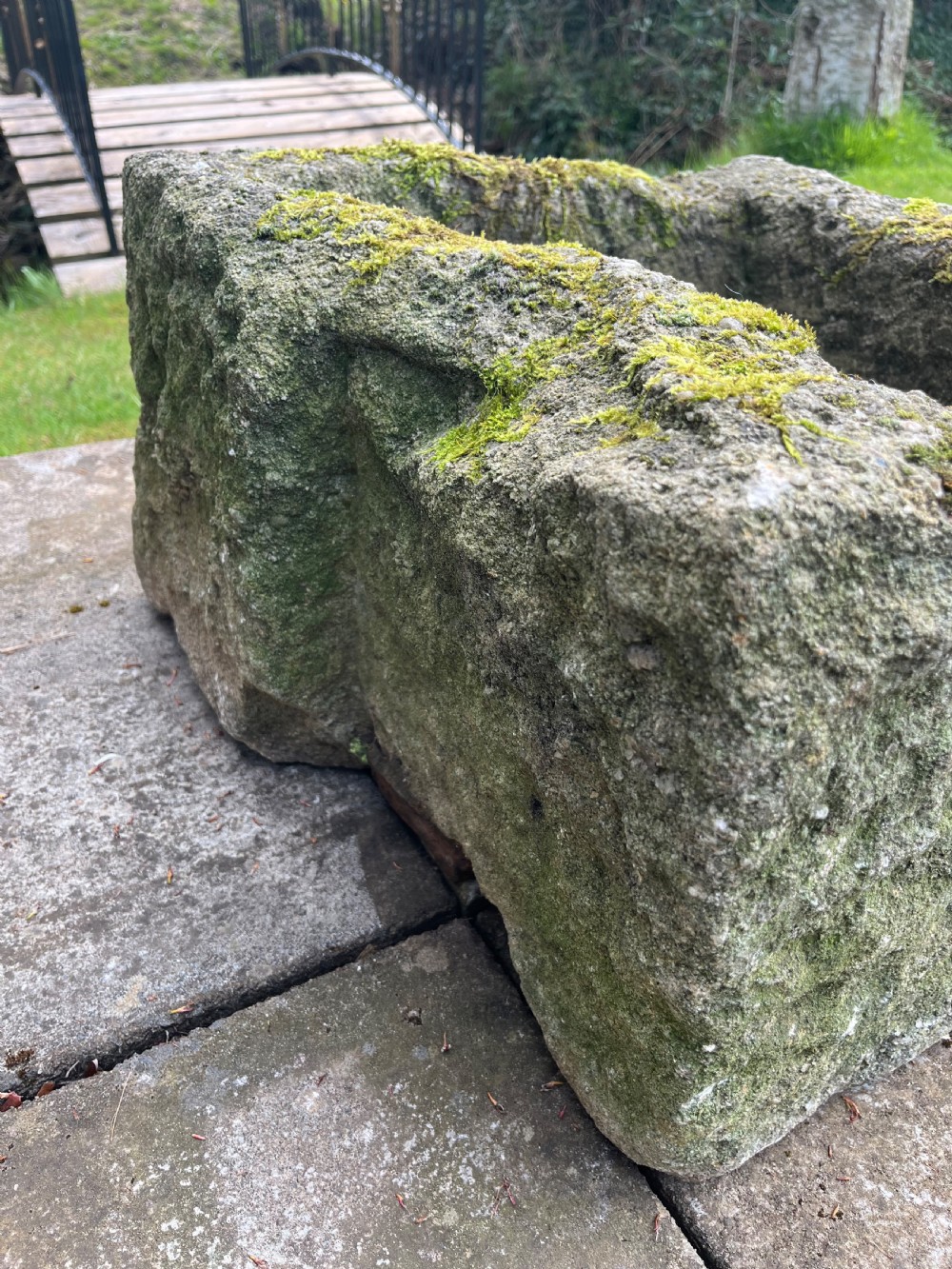 A rectangular hand-carved grey stone garden trough with a moss-covered weathered surface and a hollowed-out central basin. View III