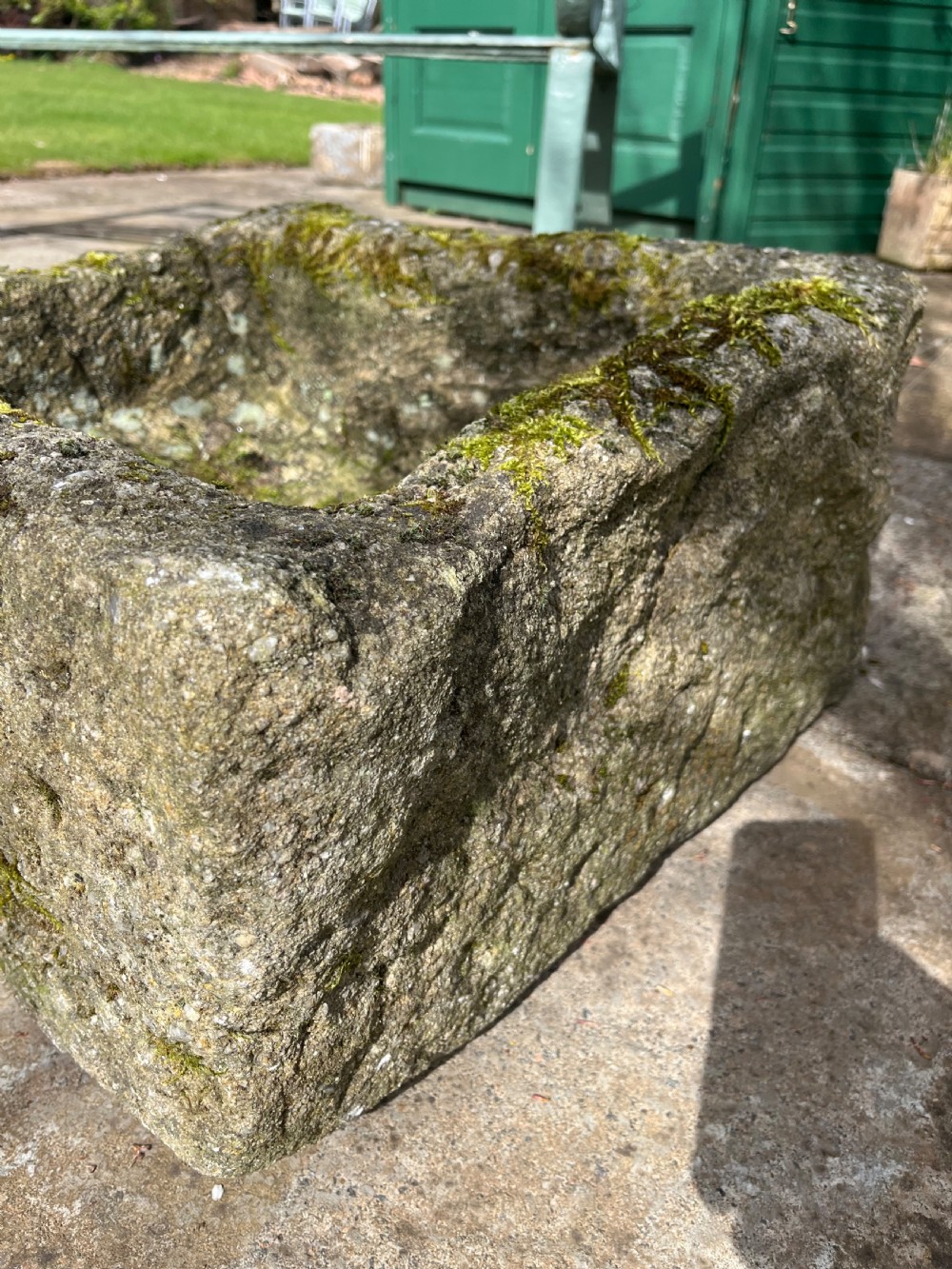 A rectangular hand-carved grey stone garden trough with a moss-covered weathered surface and a hollowed-out central basin. View V