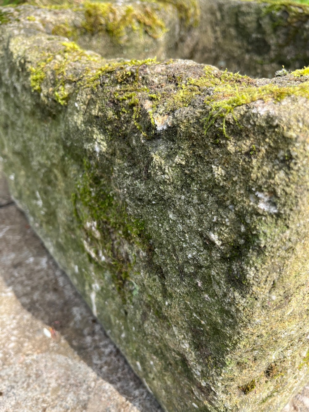 A rectangular hand-carved grey stone garden trough with a moss-covered weathered surface and a hollowed-out central basin. View VI