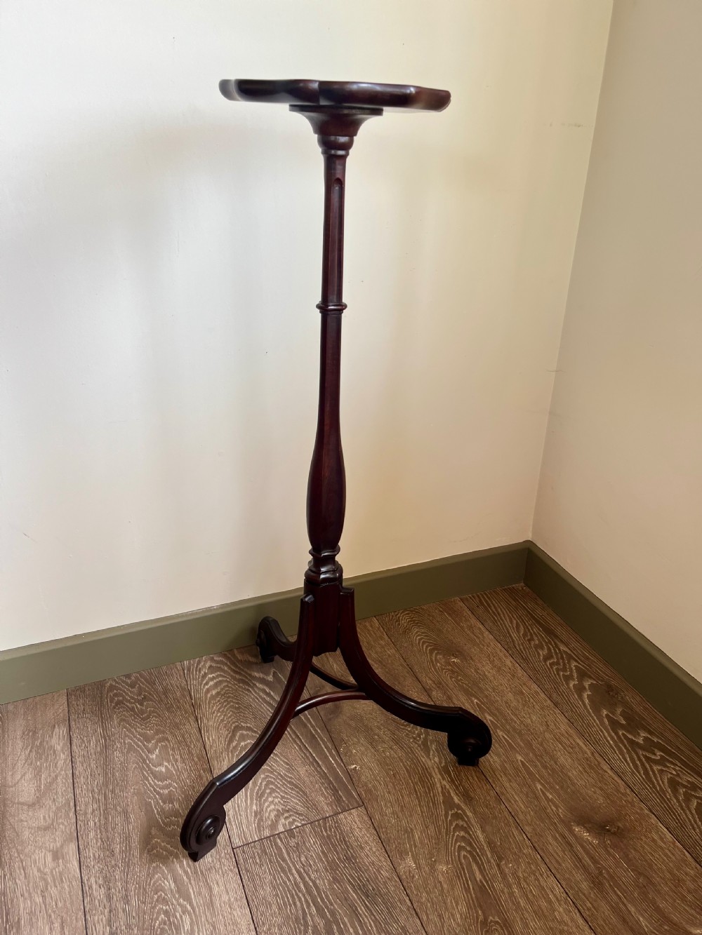 A dark mahogany torchere plant stand featuring a scalloped circular top, a turned column shaft, and a tripod base with scrolled feet.