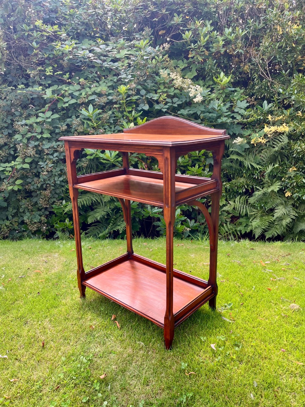 A three-tiered walnut wooden console table featuring a shaped gallery top, carved aprons, and slender tapered legs.