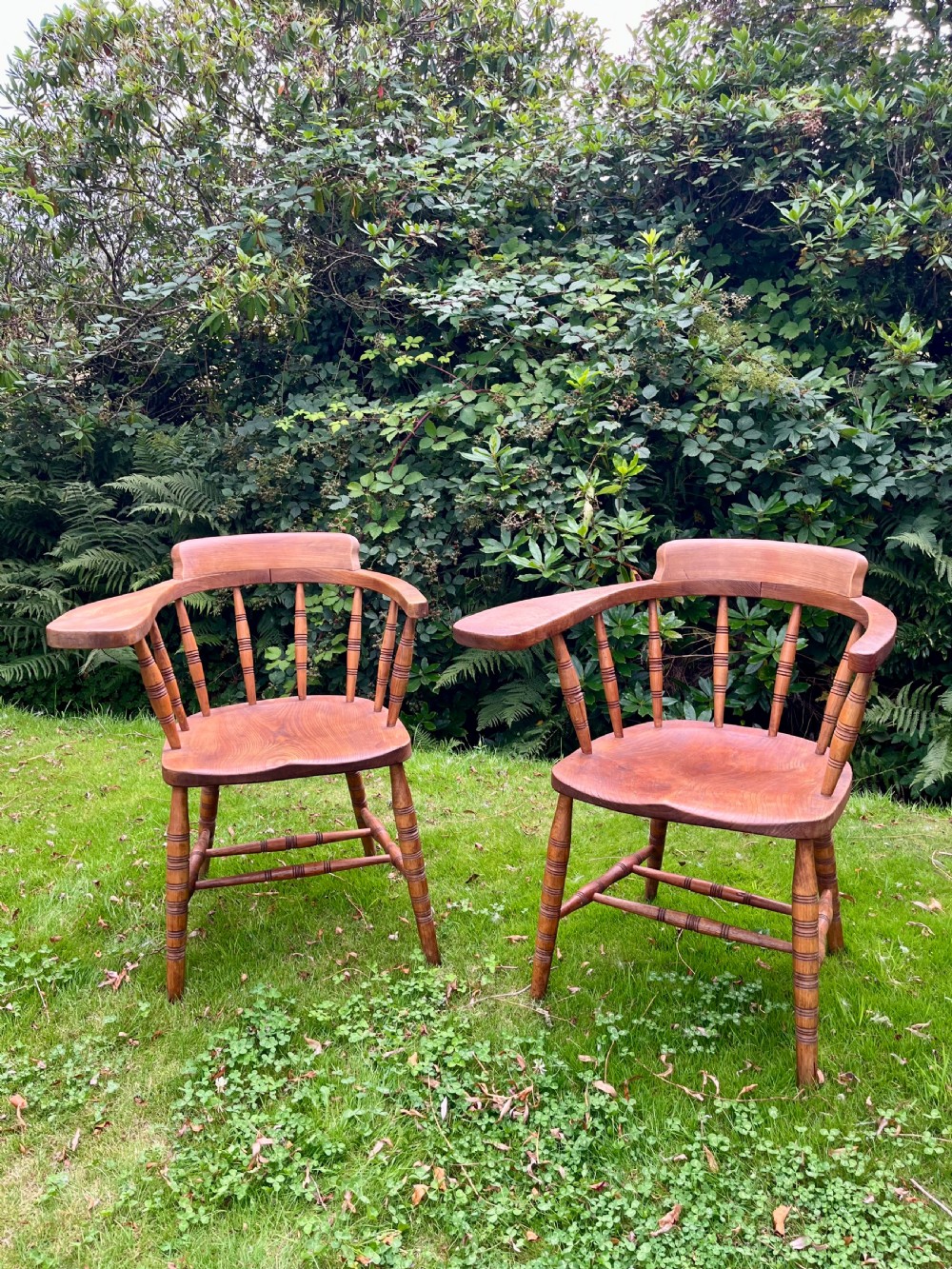 A pair of warm brown wooden smokers bow armchairs with turned spindles, contoured saddle seats, and turned legs.