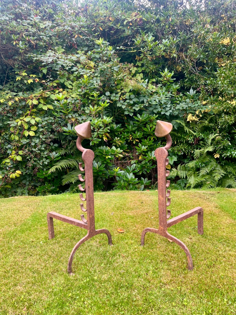 A pair of hand-forged wrought iron andirons featuring vertical spit hooks, arched feet, and conical brass finials.