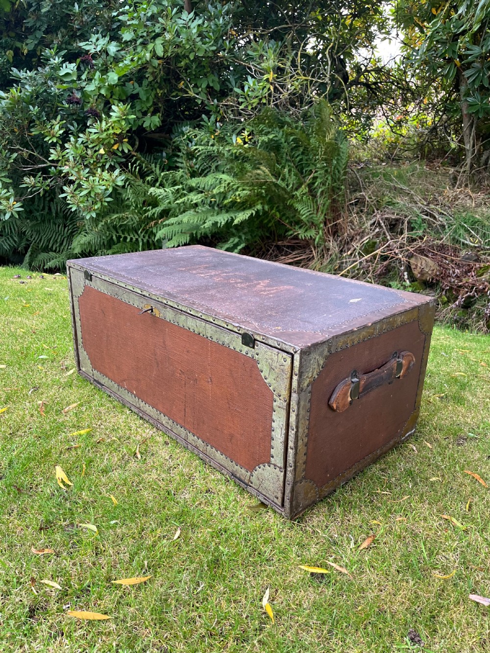 A rectangular antique dark brown canvas travel trunk featuring metal corner brackets, studding along the edges, and stencilled initials on top. View II