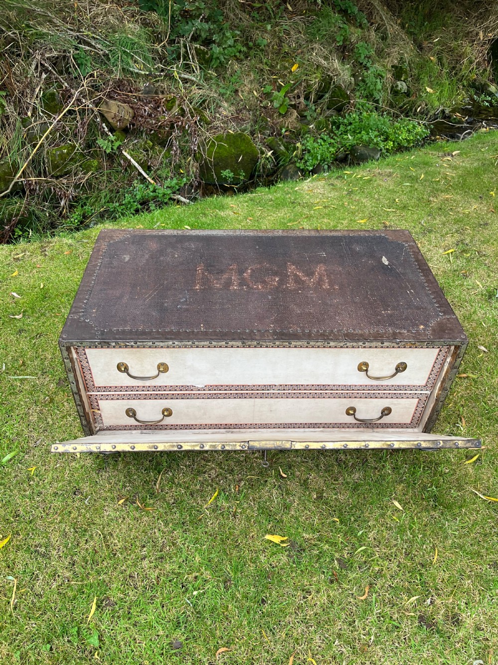 A rectangular antique dark brown canvas travel trunk featuring metal corner brackets, studding along the edges, and stencilled initials on top. View V