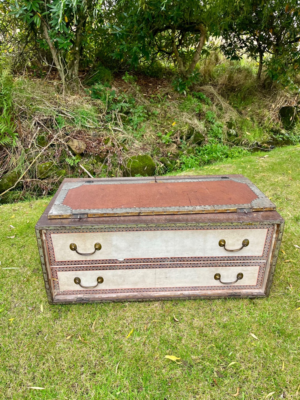A rectangular antique dark brown canvas travel trunk featuring metal corner brackets, studding along the edges, and stencilled initials on top. View VII