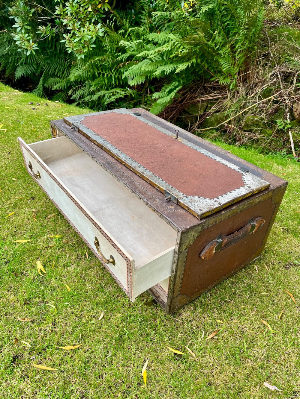 A rectangular antique dark brown canvas travel trunk featuring metal corner brackets, studding along the edges, and stencilled initials on top. View VIII