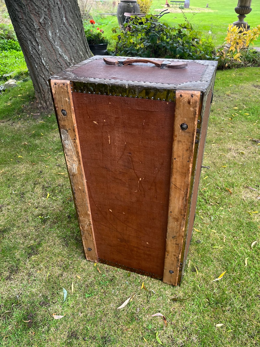 A rectangular antique dark brown canvas travel trunk featuring metal corner brackets, studding along the edges, and stencilled initials on top. View XI