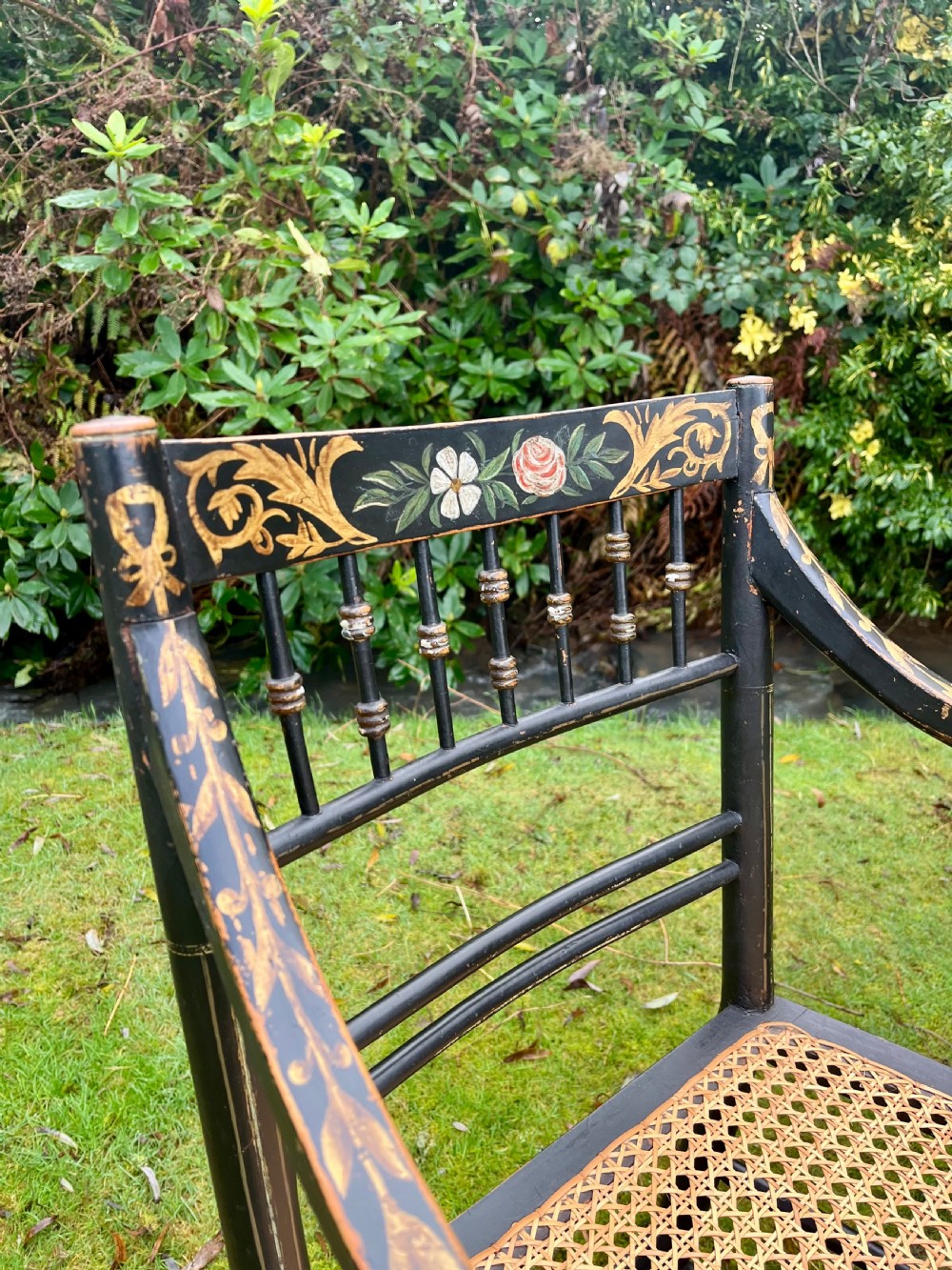 A pair of ebonised Regency armchairs featuring hand-painted floral cresting, turned spindle backs, swept arms, and woven cane seats. View III