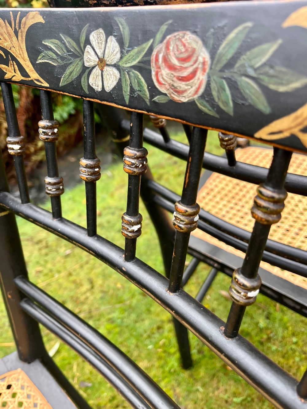 A pair of ebonised Regency armchairs featuring hand-painted floral cresting, turned spindle backs, swept arms, and woven cane seats. View XI