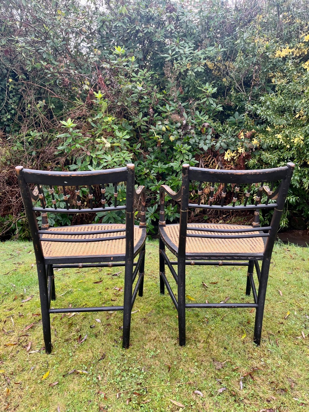A pair of ebonised Regency armchairs featuring hand-painted floral cresting, turned spindle backs, swept arms, and woven cane seats. View XII