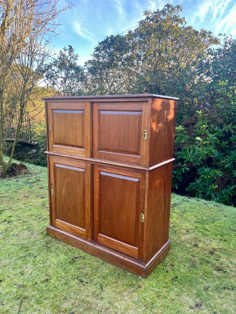 A two-part warm brown mahogany campaign cabinet featuring four panelled sliding doors with flush-fitting brass pull handles.