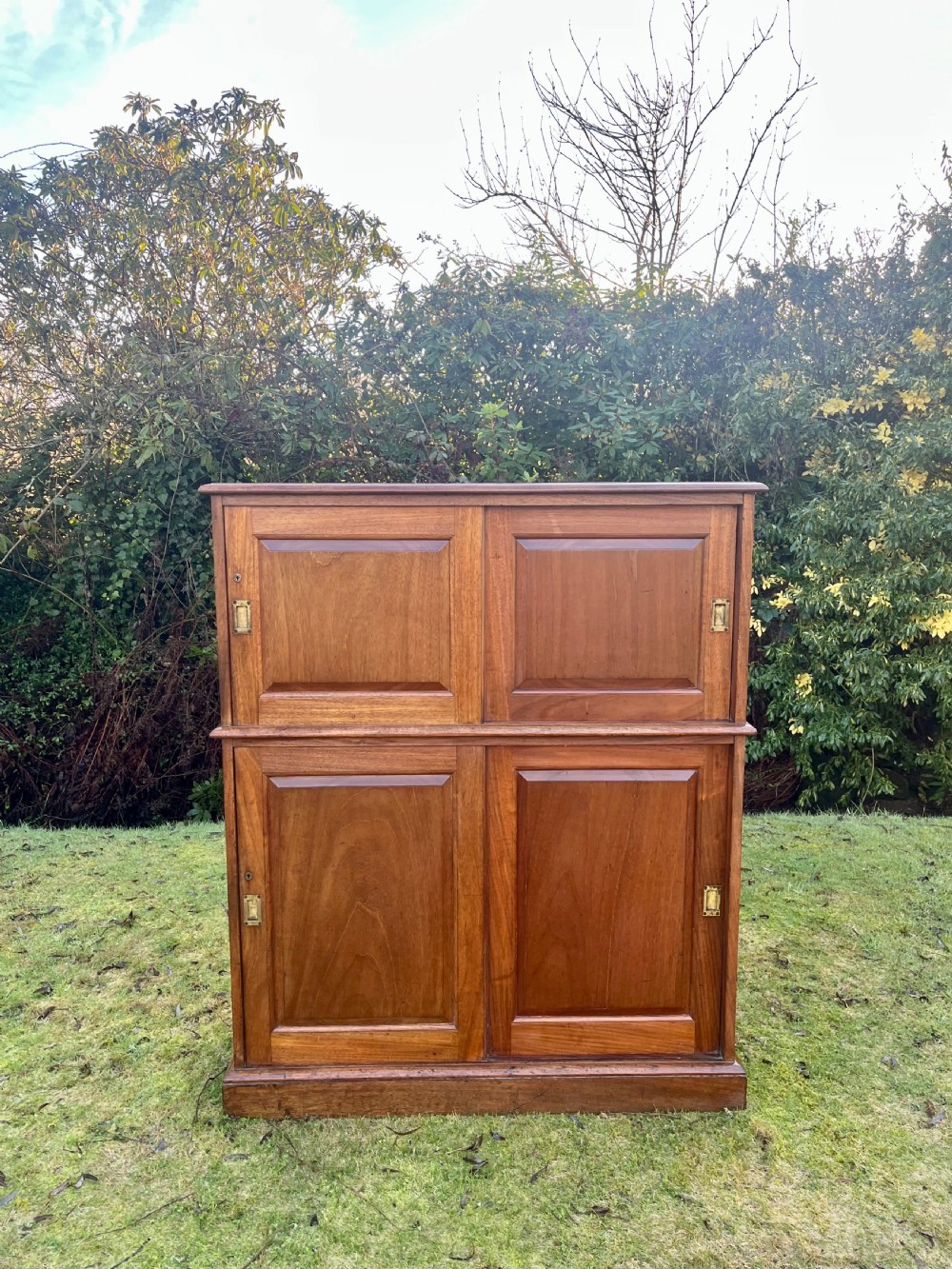 A two-part warm brown mahogany campaign cabinet featuring four panelled sliding doors with flush-fitting brass pull handles. View II