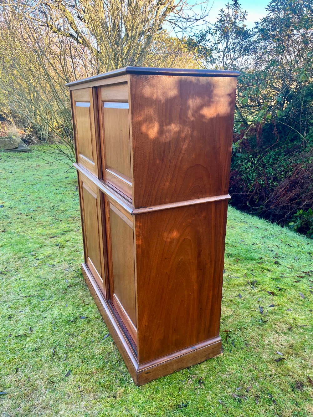 A two-part warm brown mahogany campaign cabinet featuring four panelled sliding doors with flush-fitting brass pull handles. View V