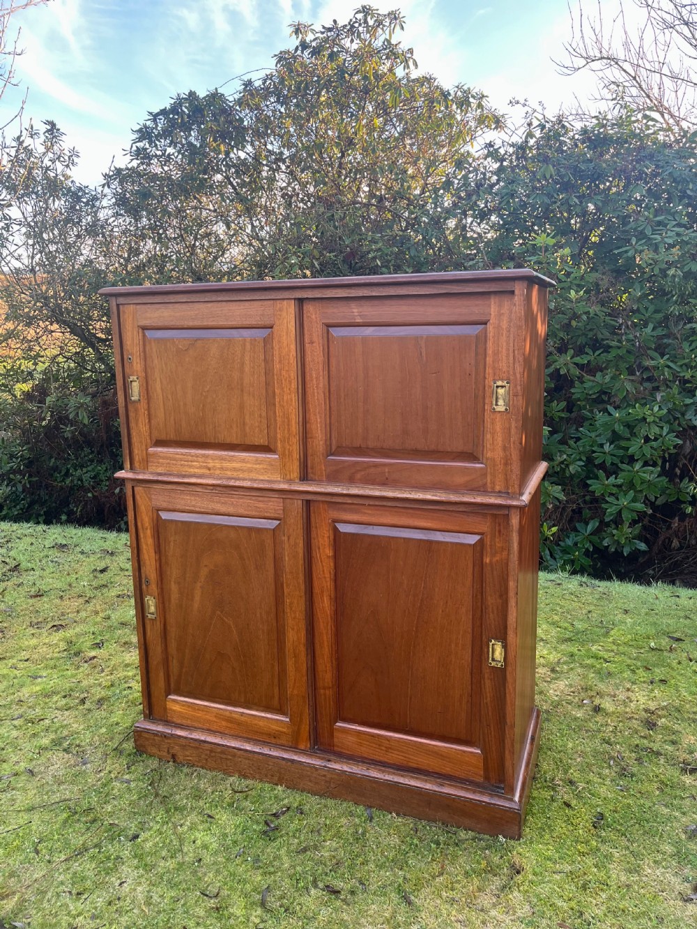 A two-part warm brown mahogany campaign cabinet featuring four panelled sliding doors with flush-fitting brass pull handles. View XV
