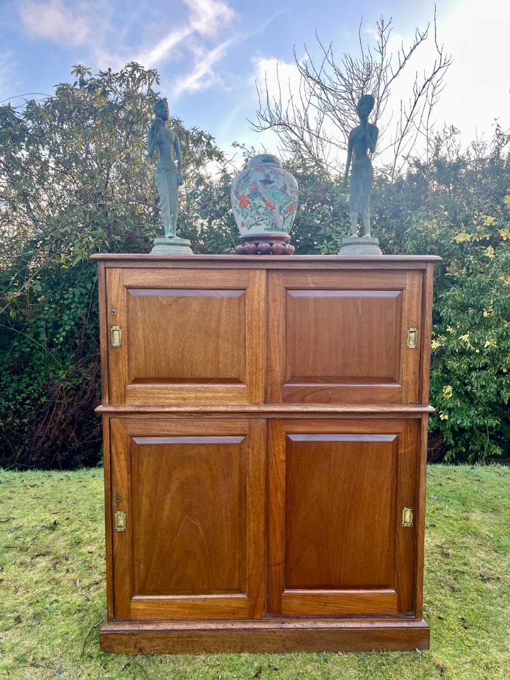 A two-part warm brown mahogany campaign cabinet featuring four panelled sliding doors with flush-fitting brass pull handles. View XVI