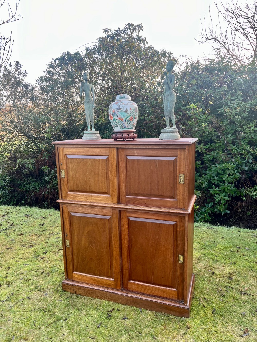 A two-part warm brown mahogany campaign cabinet featuring four panelled sliding doors with flush-fitting brass pull handles. View XVII