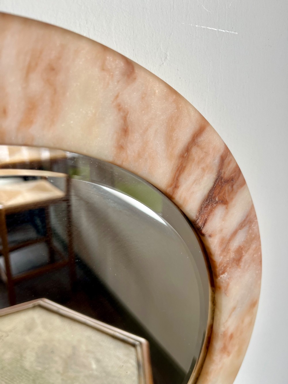 A circular wall mirror featuring a thick alabaster stone frame with visible pink and cream veining surrounding bevelled mirror glass. View II