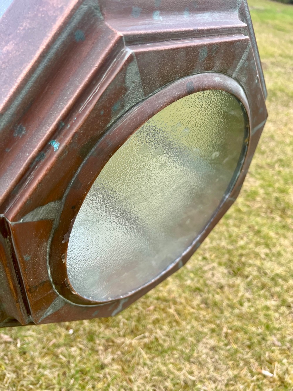 A large octagonal copper wall lantern with textured glass panels mounted on a grey metal bracket. View IX