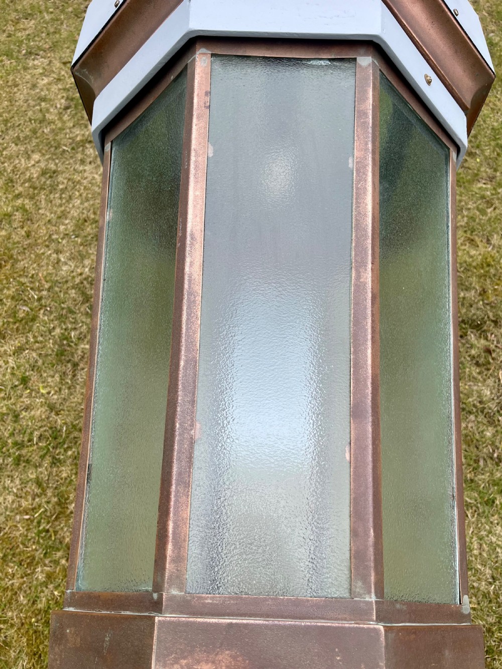 A large octagonal copper wall lantern with textured glass panels mounted on a grey metal bracket. View XII