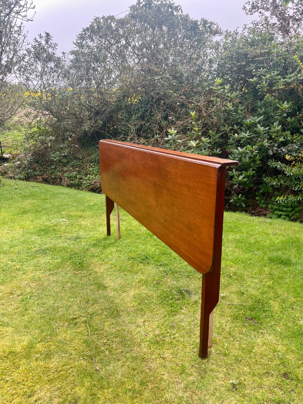 A long, narrow antique wooden butlers console table with a polished warm brown finish, rounded corners, and a collapsible trestle leg frame. View II