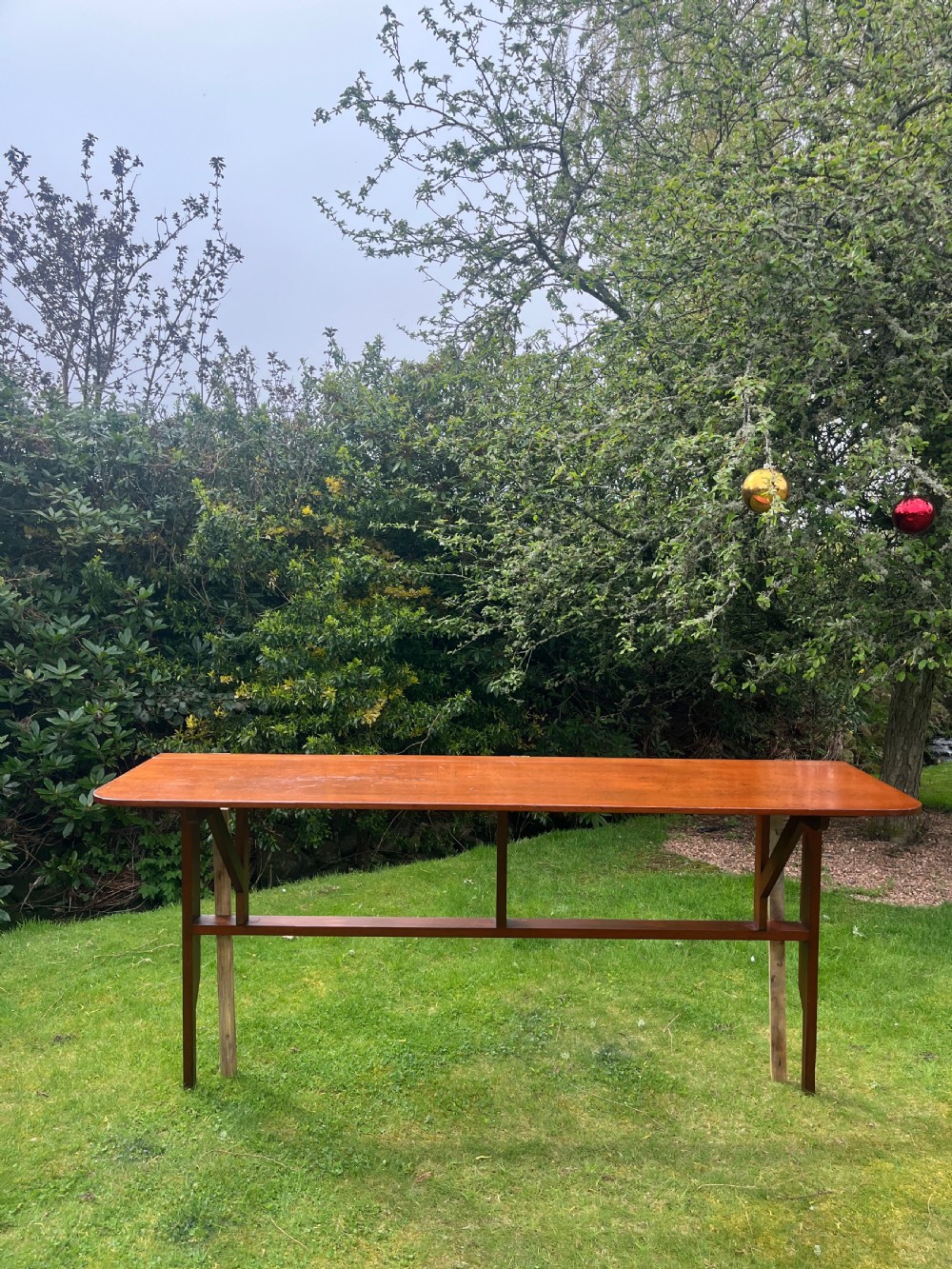 A long, narrow antique wooden butlers console table with a polished warm brown finish, rounded corners, and a collapsible trestle leg frame. View V