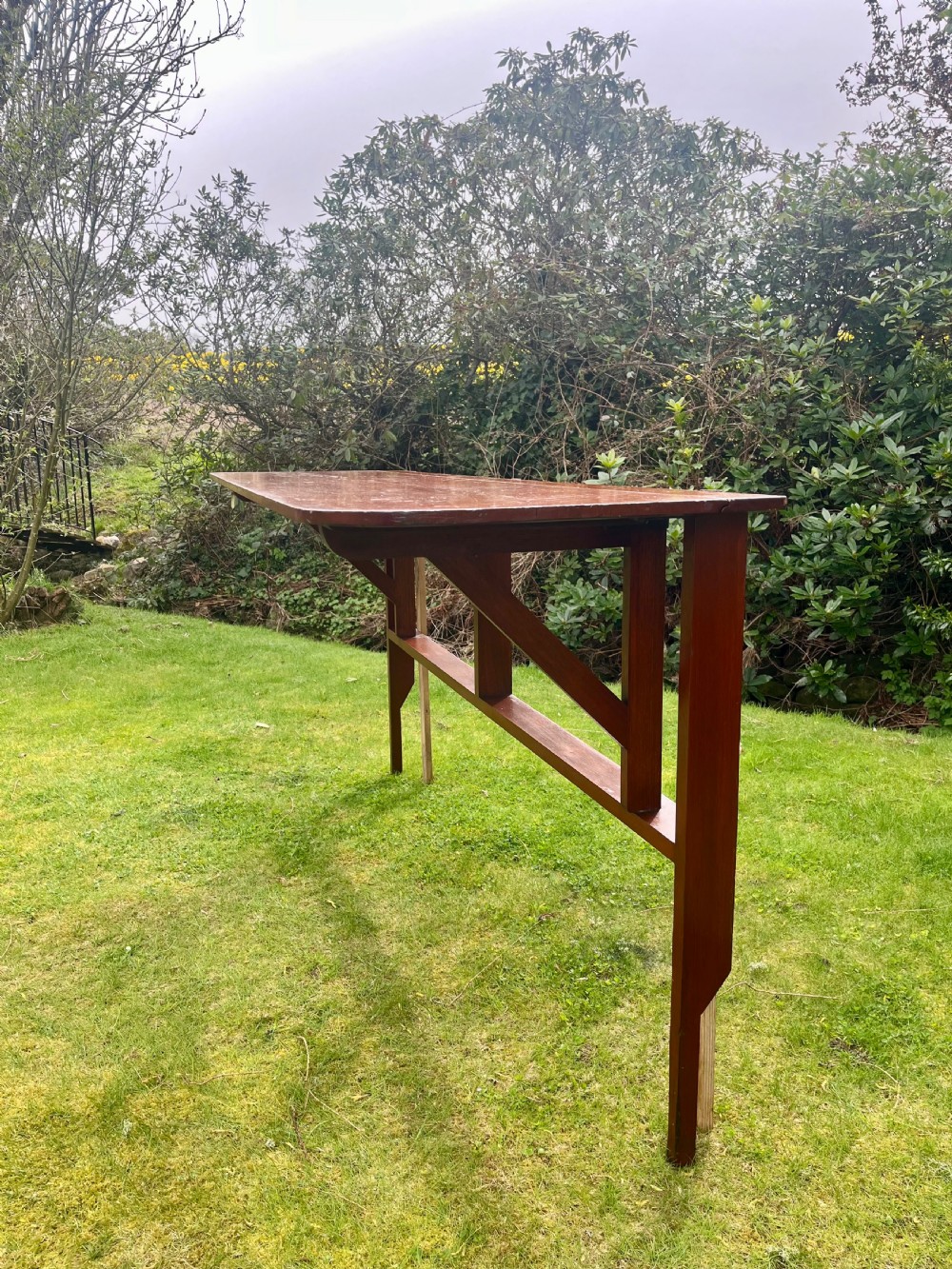 A long, narrow antique wooden butlers console table with a polished warm brown finish, rounded corners, and a collapsible trestle leg frame. View VI